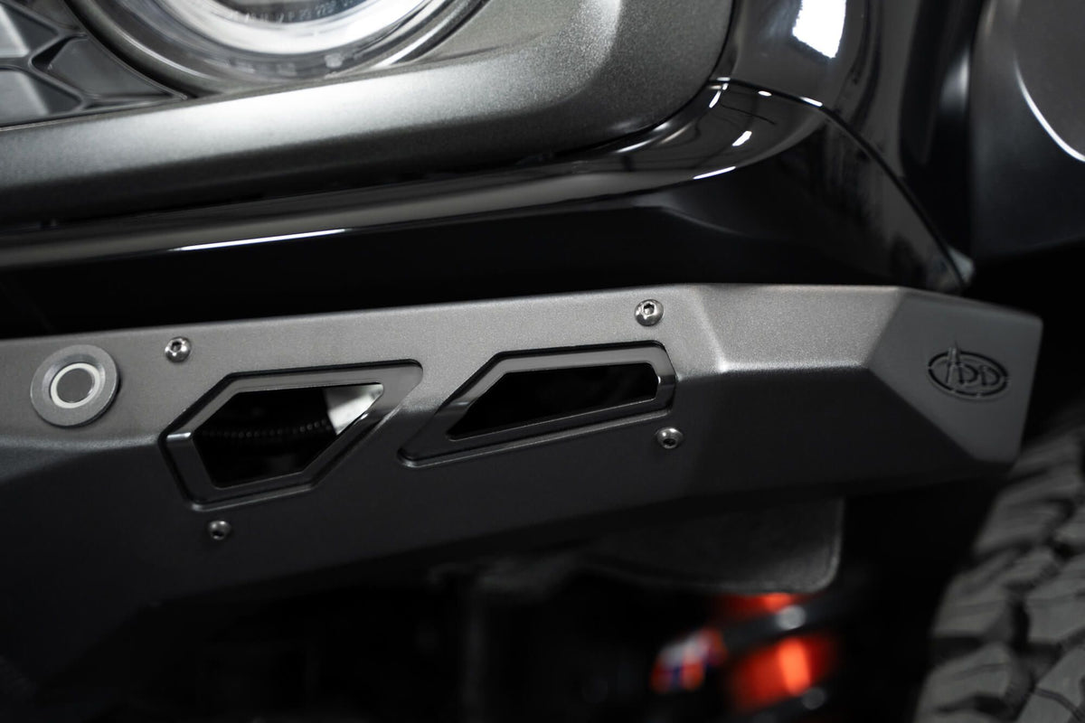 Addictive Desert Designs Phantom front bumper installed on black Ford Bronco Raptor, close-up showing bumper corner and wheel well