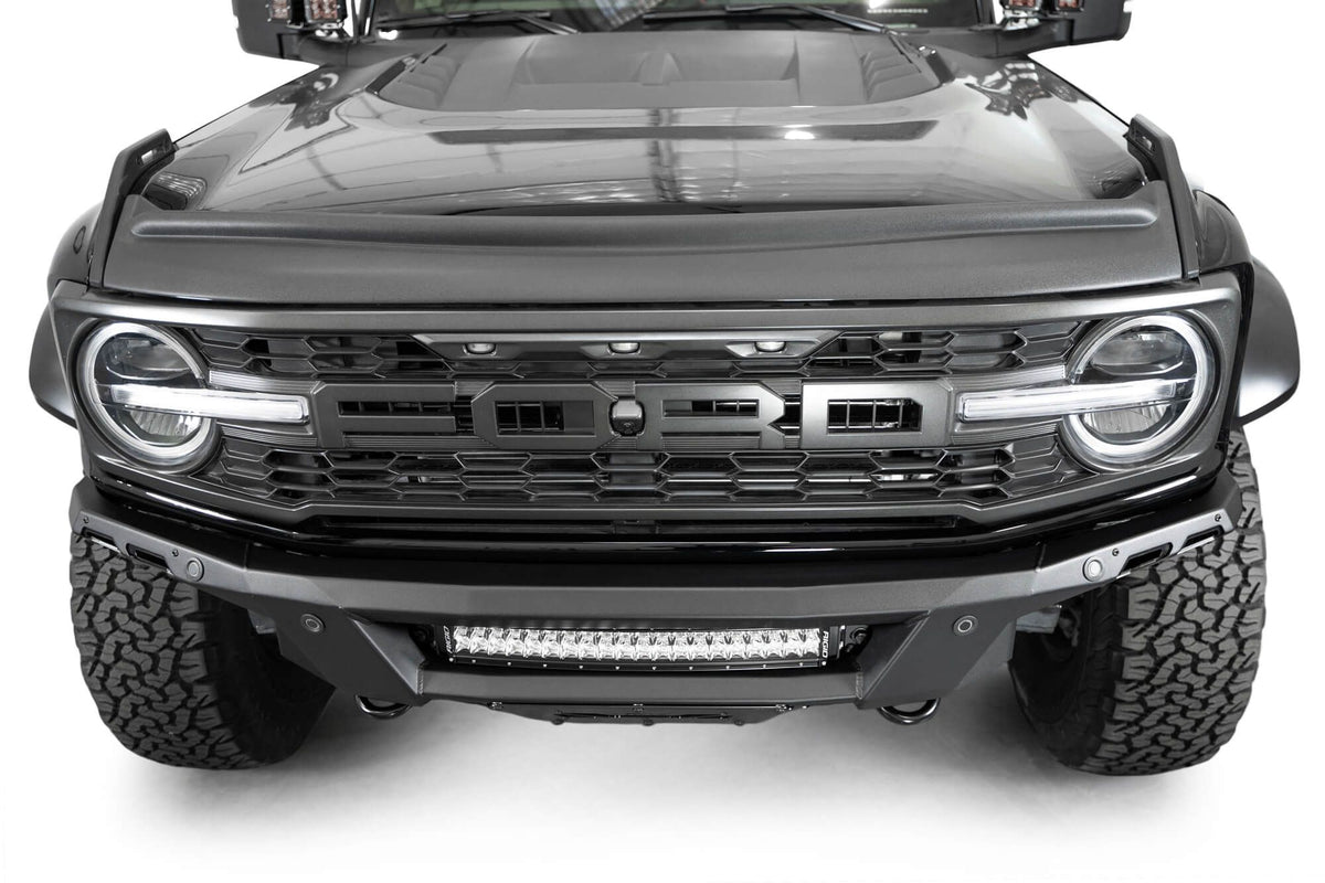 Addictive Desert Designs Phantom front bumper installed on black Ford Bronco Raptor, straight-on close-up showing grille, headlight, and light bar
