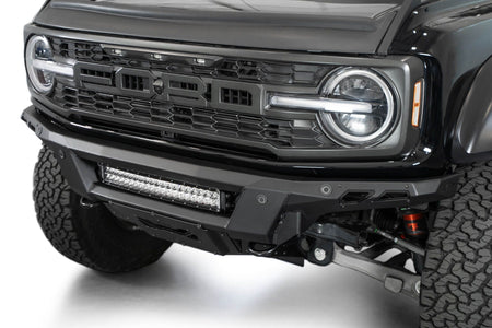 Addictive Desert Designs Phantom front bumper installed on black Ford Bronco Raptor, close-up showing grille, headlight, and integrated light bar
