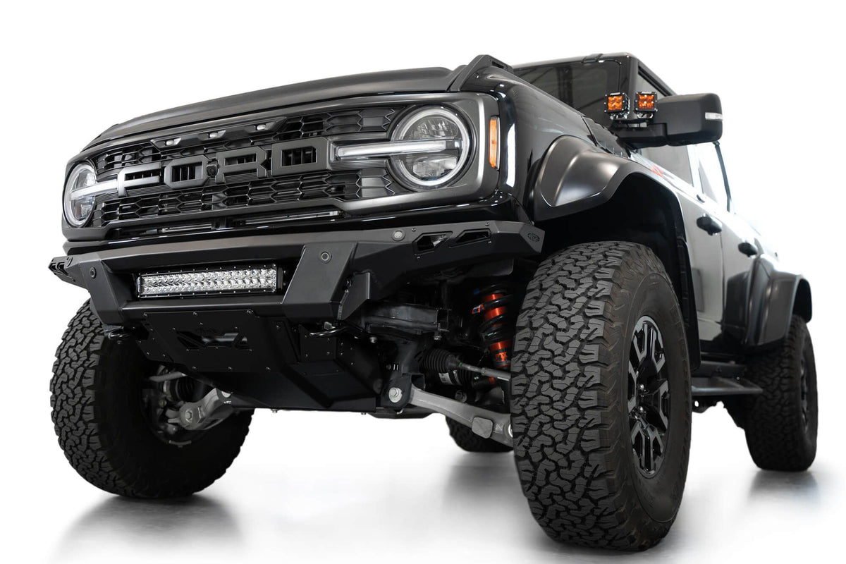 Addictive Desert Designs Phantom front bumper installed on black Ford Bronco Raptor, front three-quarter view of full vehicle with roof rack, product shot on white background