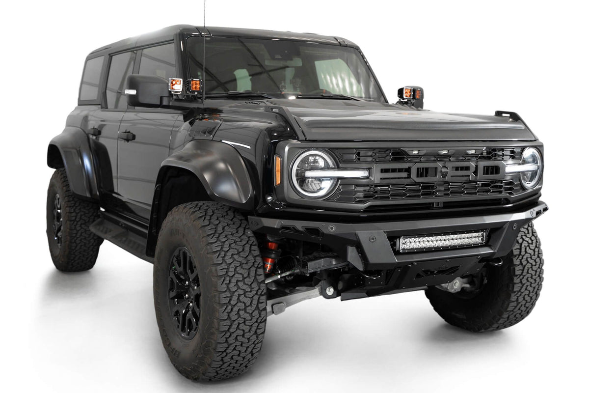 Addictive Desert Designs Phantom front bumper installed on black Ford Bronco Raptor, front three-quarter view with roof rack and marker lights, product shot on white background, alternate angle