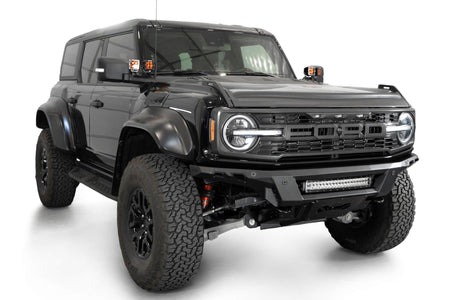 Addictive Desert Designs Phantom front bumper installed on black Ford Bronco Raptor, front three-quarter view with roof rack and marker lights, product shot on white background, alternate angle
