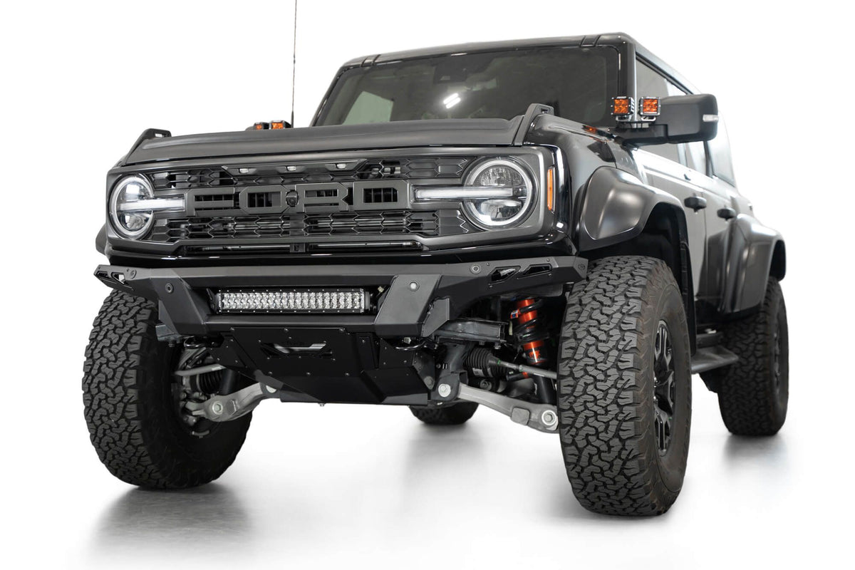 Addictive Desert Designs Phantom front bumper installed on black Ford Bronco Raptor, front three-quarter view with roof rack and marker lights, product shot on white background