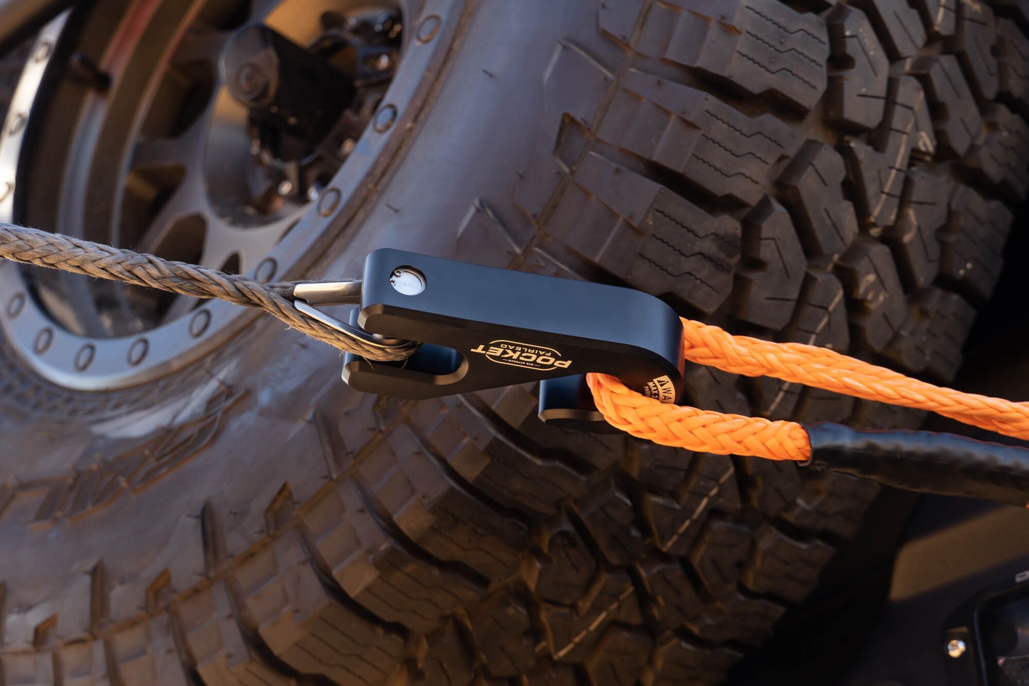 Close-up of a fairlead hooked around an orange rope with a vehicle tire in the background