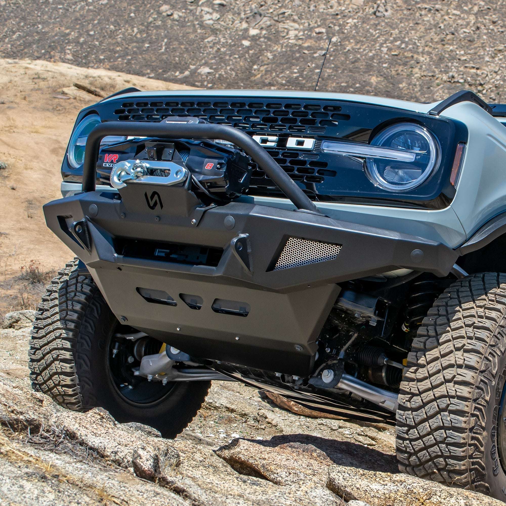 Turn Offroad winch front bumper package installed on Ford Bronco, front three-quarter view showing skid plate and suspension on rocky terrain