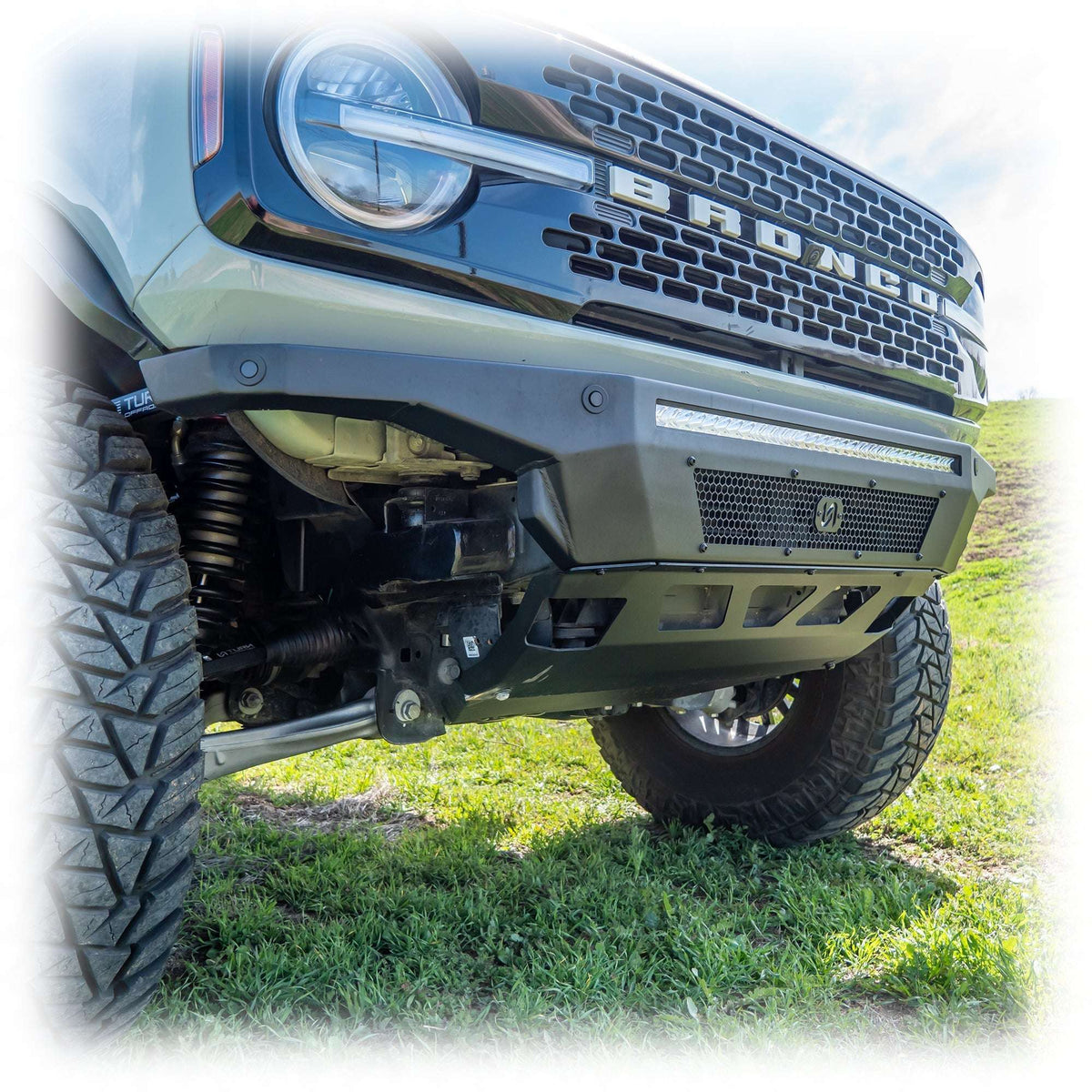 Turn Offroad Hyperlyte front bumper installed on olive green Ford Bronco, close-up showing bumper and wheel on hillside