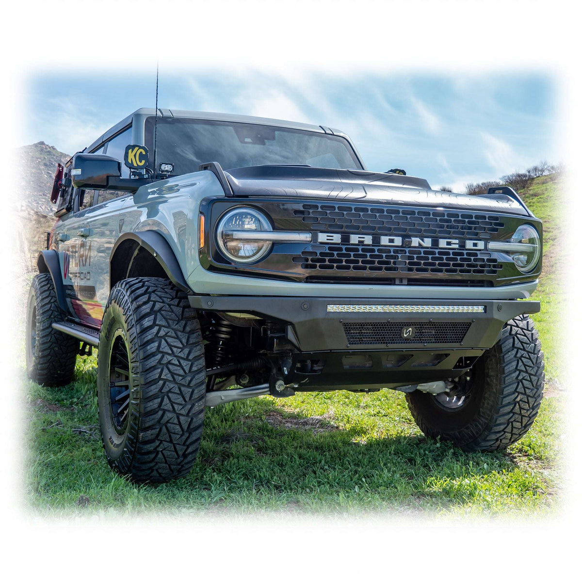 Turn Offroad Hyperlyte front bumper installed on olive green Ford Bronco, distant front three-quarter view of full vehicle on mountain terrain