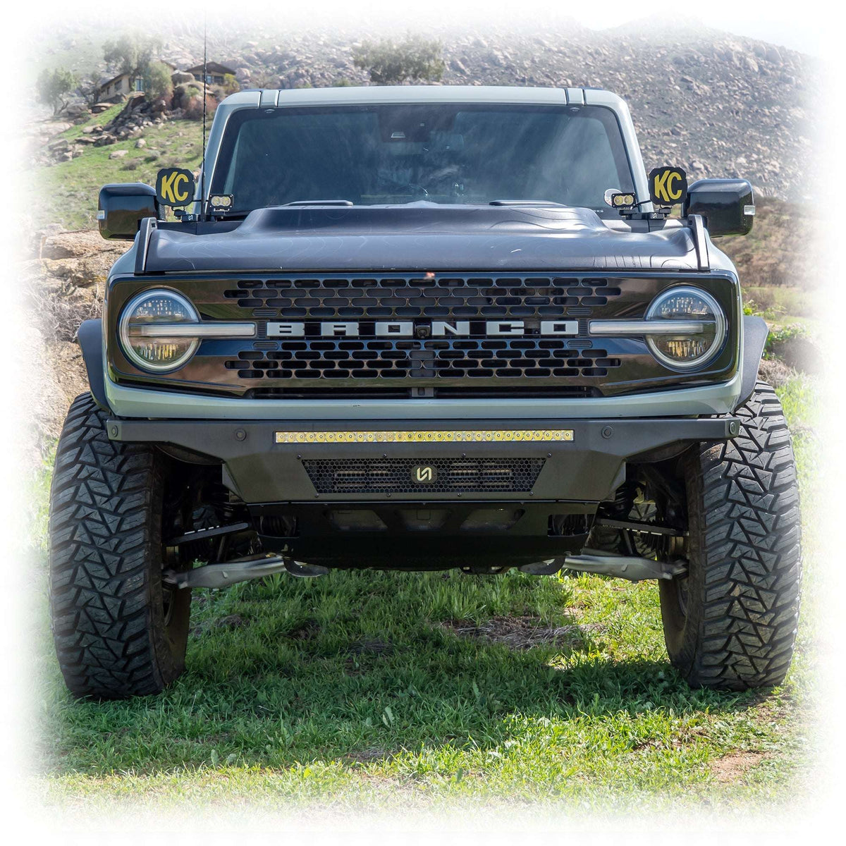 Turn Offroad Hyperlyte front bumper installed on black Ford Bronco with KC light pods, straight-on front view in grass field, alternate angle