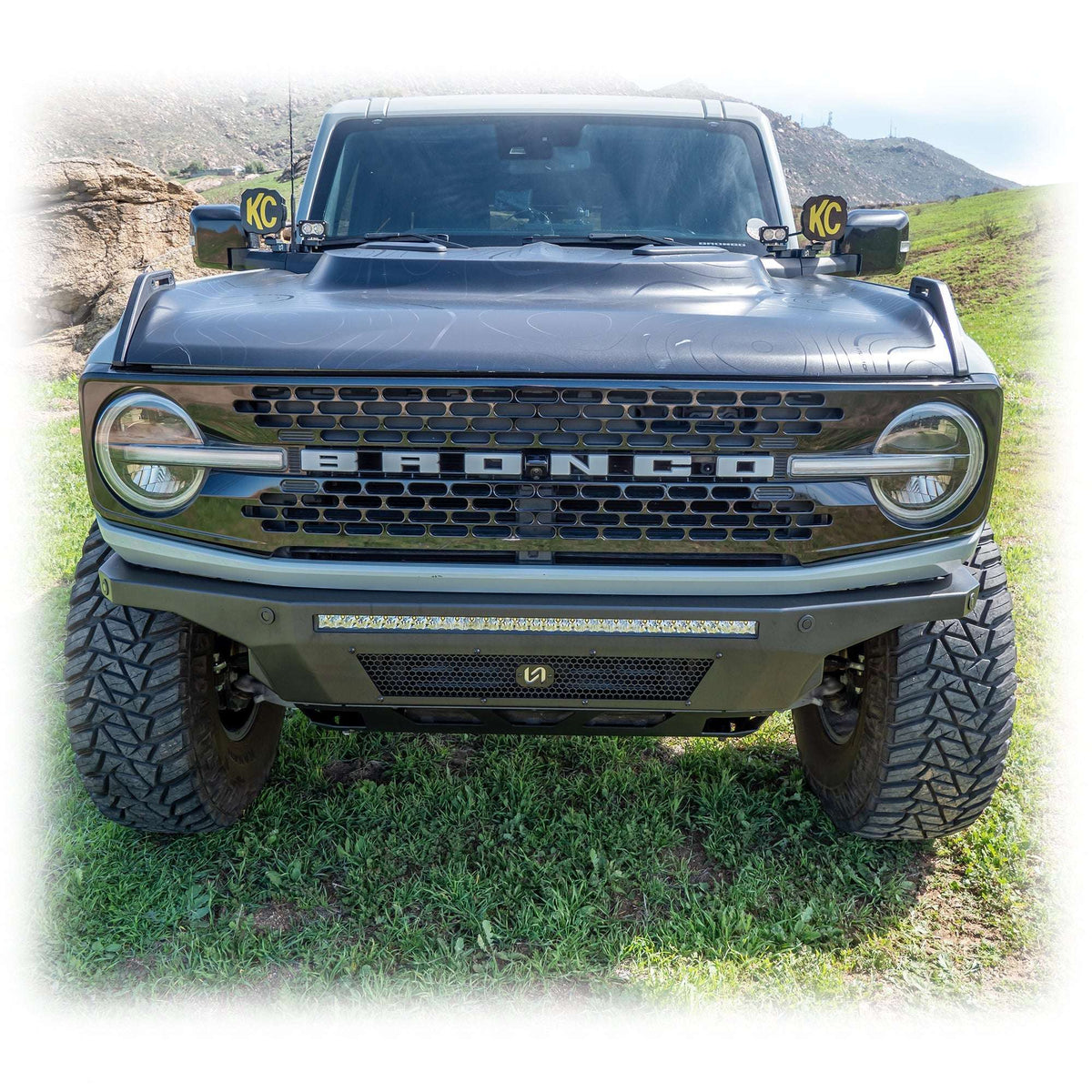 Turn Offroad Hyperlyte front bumper installed on black Ford Bronco with KC light pods, straight-on front view in grass field
