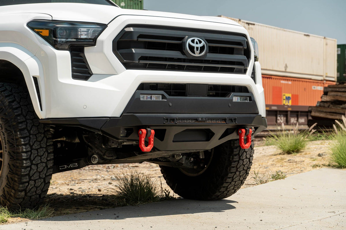 DV8 Offroad front bumper compatible with FBBO-01 fairlead cover plate, close front three-quarter view near railroad tracks