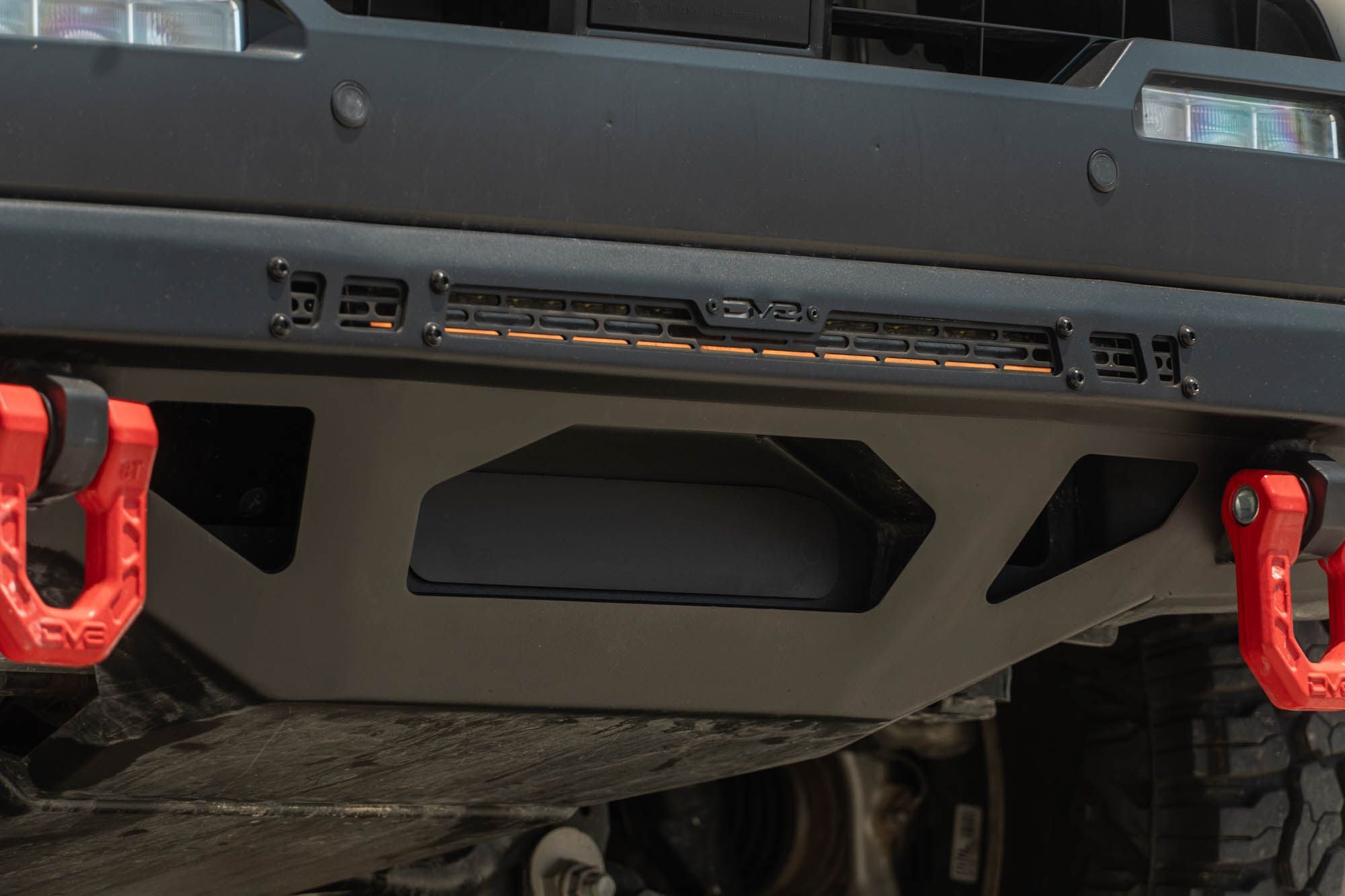 DV8 Offroad front bumper compatible with FBBO-01 fairlead cover plate, close-up showing red D-ring recovery shackle mount and skid plate