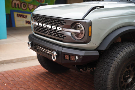 DV8 Offroad OE Plus Series front bumper installed on silver Ford Bronco, front three-quarter close-up with colorful mural background