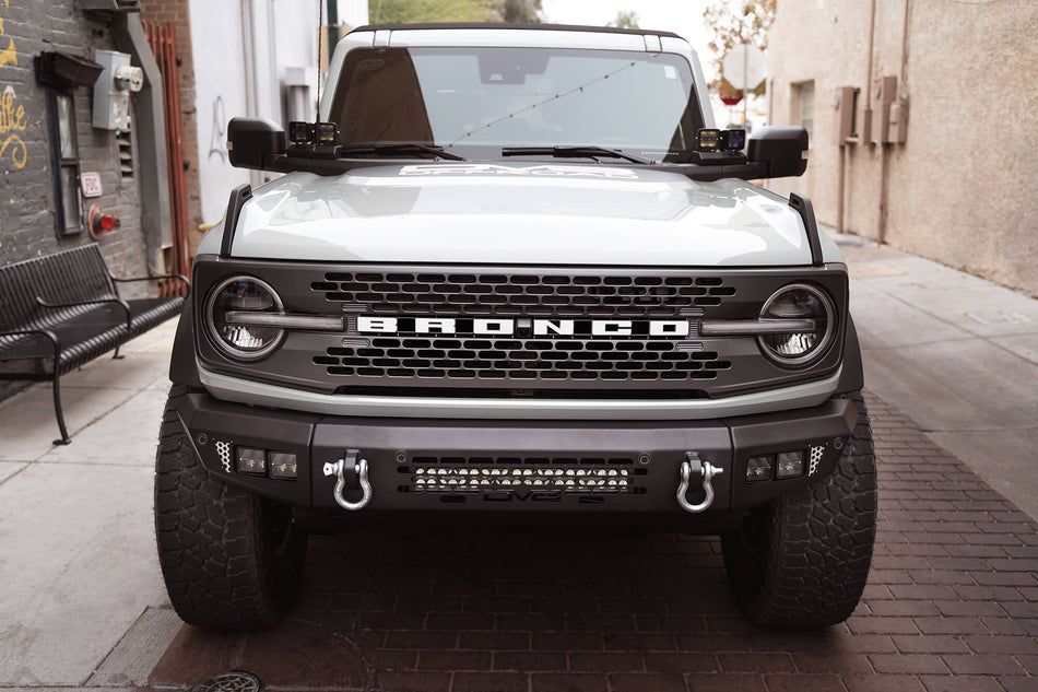 DV8 Offroad OE Plus Series front bumper installed on silver Ford Bronco, straight-on front view in urban setting