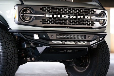 DV8 Offroad Competition Series front bumper installed on dark Ford Bronco, close-up showing bumper corner and wheel in parking garage, alternate angle