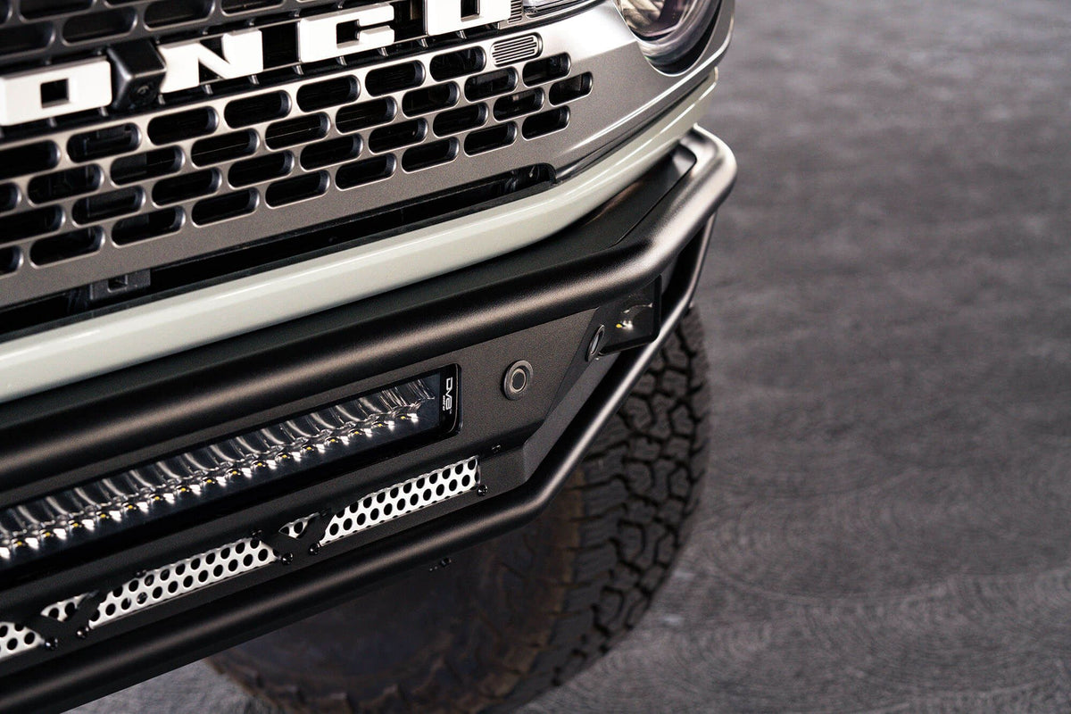 DV8 Offroad Competition Series front bumper installed on light-colored Ford Bronco, close-up front view in urban setting