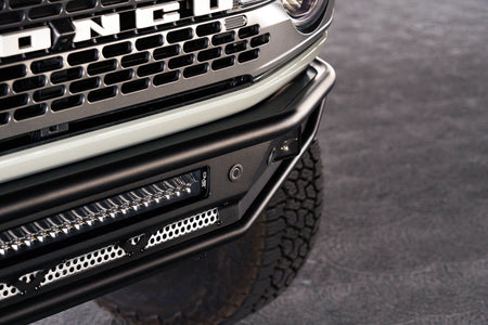 DV8 Offroad Competition Series front bumper installed on light-colored Ford Bronco, close-up front view in urban setting