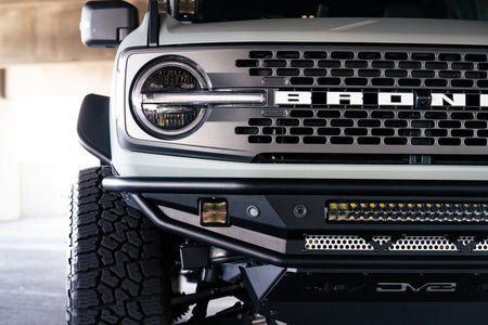 DV8 Offroad Competition Series front bumper installed on dark green Ford Bronco, close-up showing grille and bumper in parking garage