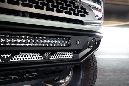 DV8 Offroad Competition Series front bumper installed on light-colored Ford Bronco, close-up showing grille and light bar in parking garage