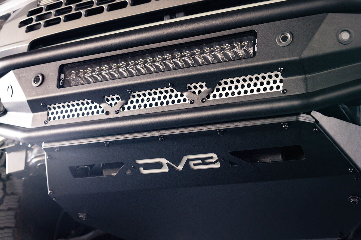 DV8 Offroad Competition Series front bumper installed on Ford Bronco, close-up showing skid plate, light bar and DV8 logo in parking garage