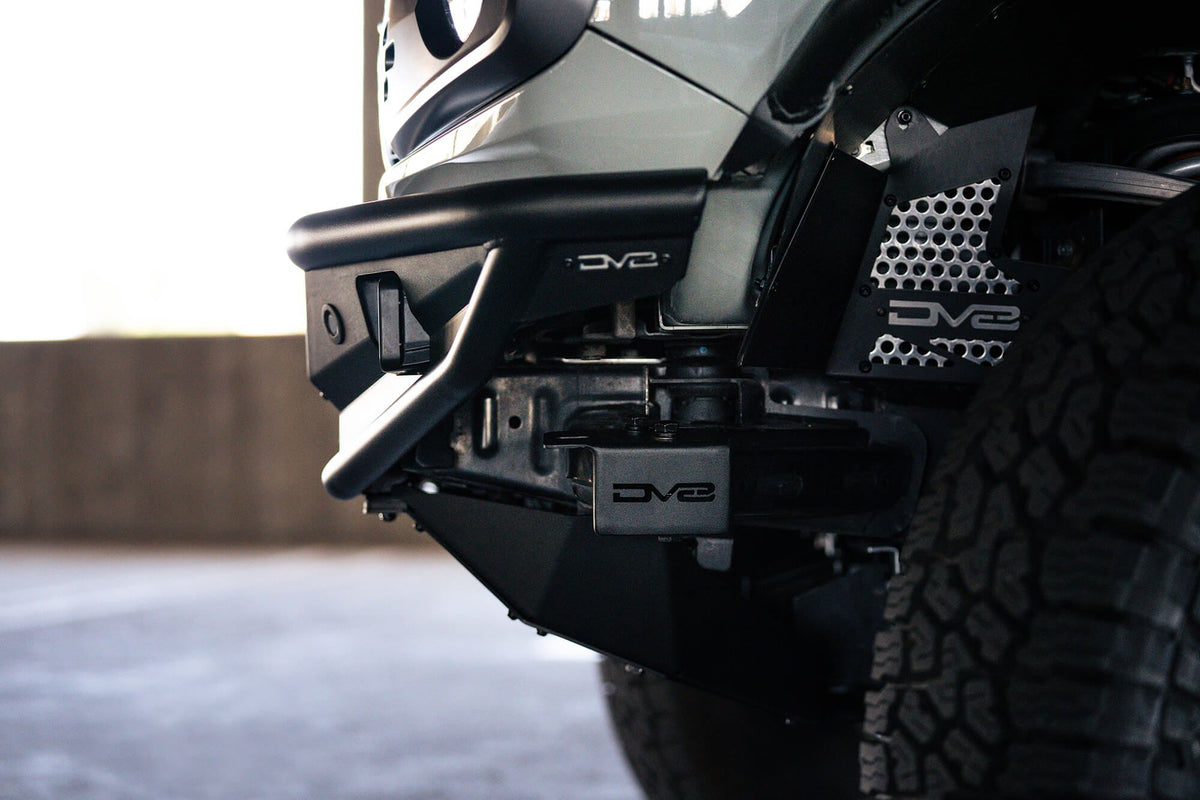 DV8 Offroad Competition Series front bumper installed on white Ford Bronco, close-up showing bumper corner and wheel in parking garage