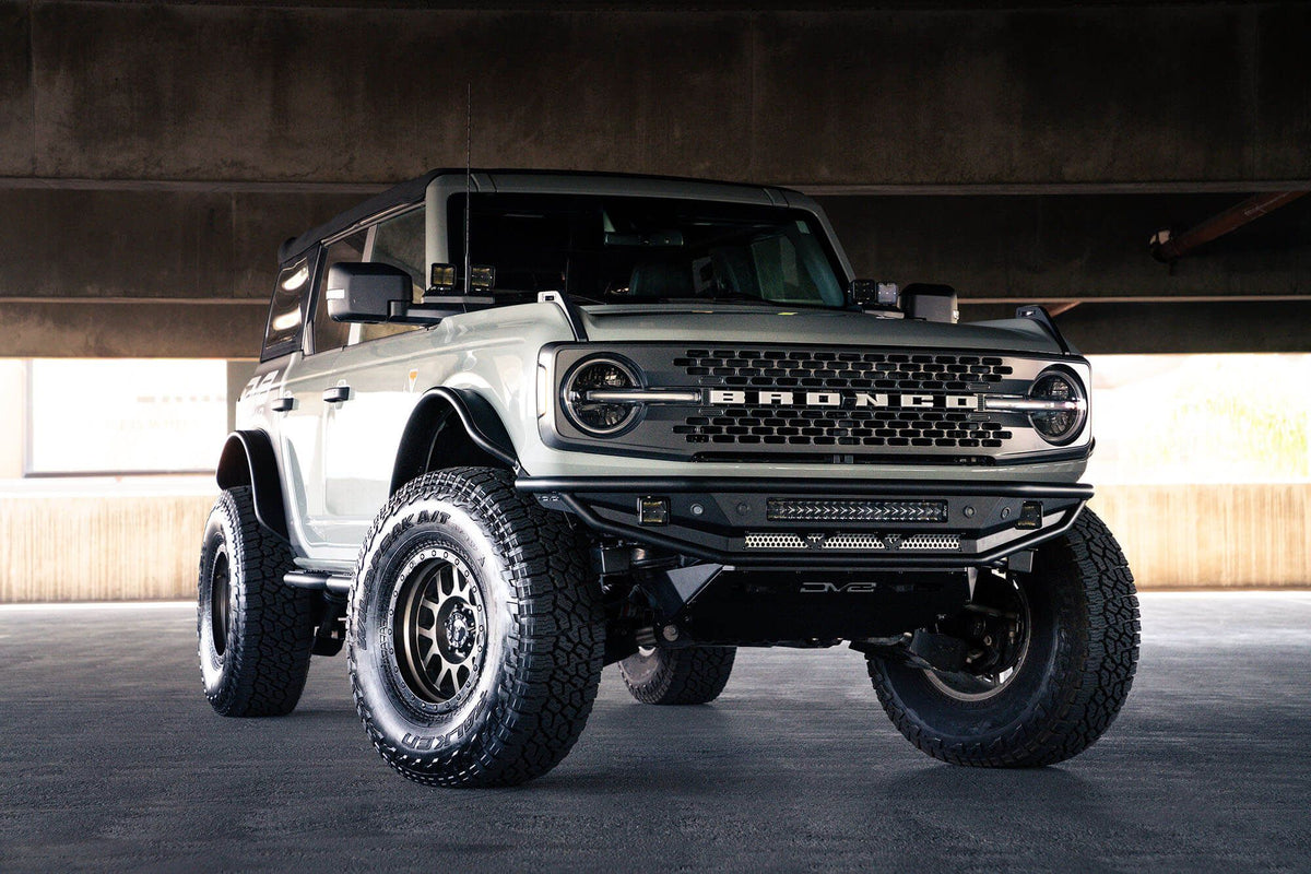DV8 Offroad Competition Series front bumper installed on dark Ford Bronco, distant front three-quarter view of full vehicle in parking garage