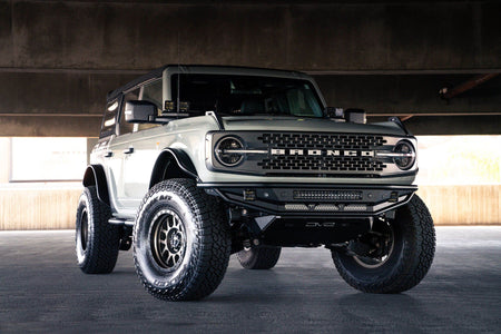 DV8 Offroad Competition Series front bumper installed on dark Ford Bronco, distant front three-quarter view of full vehicle in parking garage