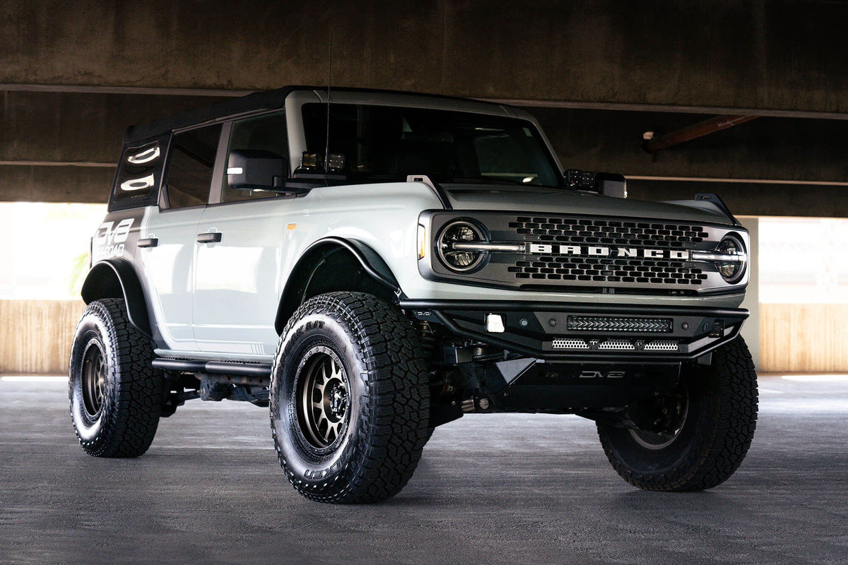 DV8 Offroad Competition Series front bumper installed on white Ford Bronco, distant front three-quarter view of full vehicle in parking garage