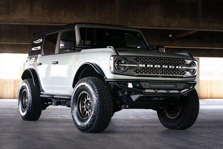 DV8 Offroad Competition Series front bumper installed on white Ford Bronco, distant front three-quarter view of full vehicle in parking garage