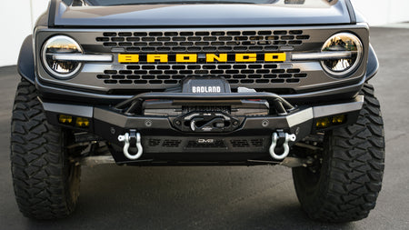 DV8 Offroad Spec Series winch front bumper installed on dark green Ford Bronco Badlands, straight-on front view showing D-ring shackles
