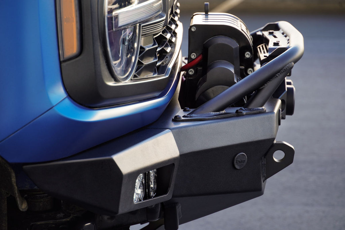 DV8 Offroad Spec Series winch front bumper installed on blue Ford Bronco, close-up showing bumper corner and headlight in parking lot
