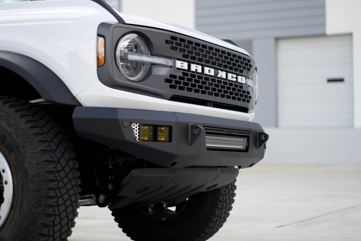DV8 Offroad OE Plus Series V2 front bumper installed on white Ford Bronco, close-up front view in urban lot
