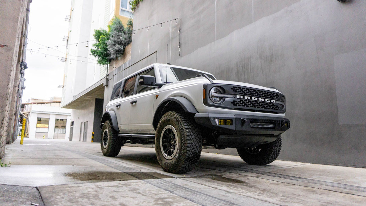 DV8 Offroad OE Plus Series V2 front bumper installed on gray Ford Bronco, distant front three-quarter view on urban street