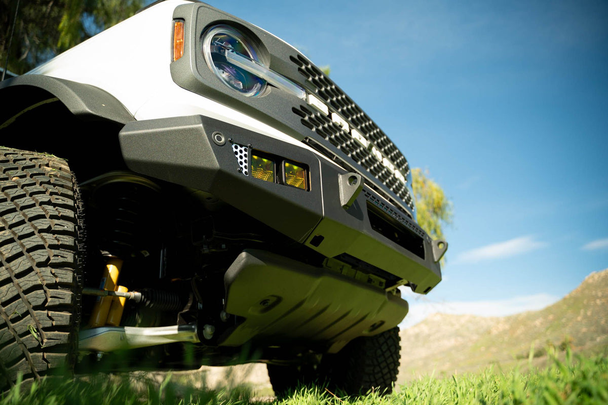 DV8 Offroad OE Plus Series V2 front bumper installed on olive green Ford Bronco, low-angle close-up showing bumper and wheel