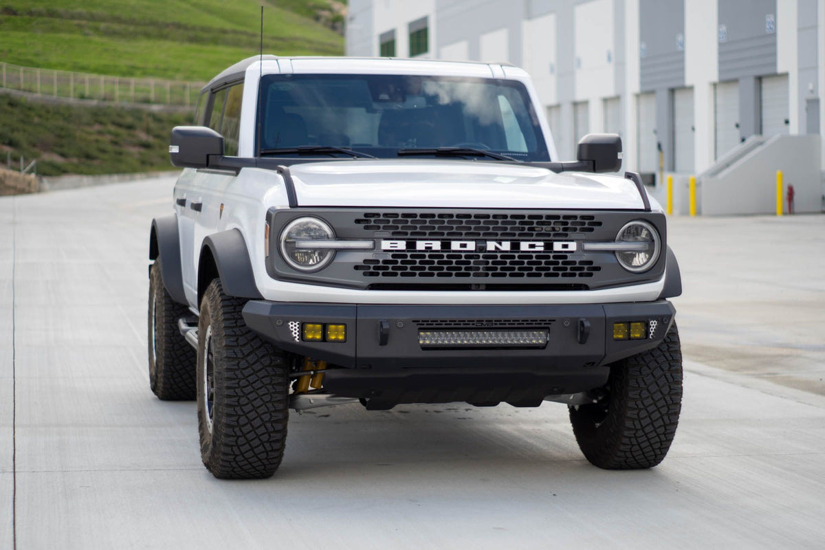 DV8 Offroad OE Plus Series V2 front bumper installed on white Ford Bronco, straight-on front view in industrial lot