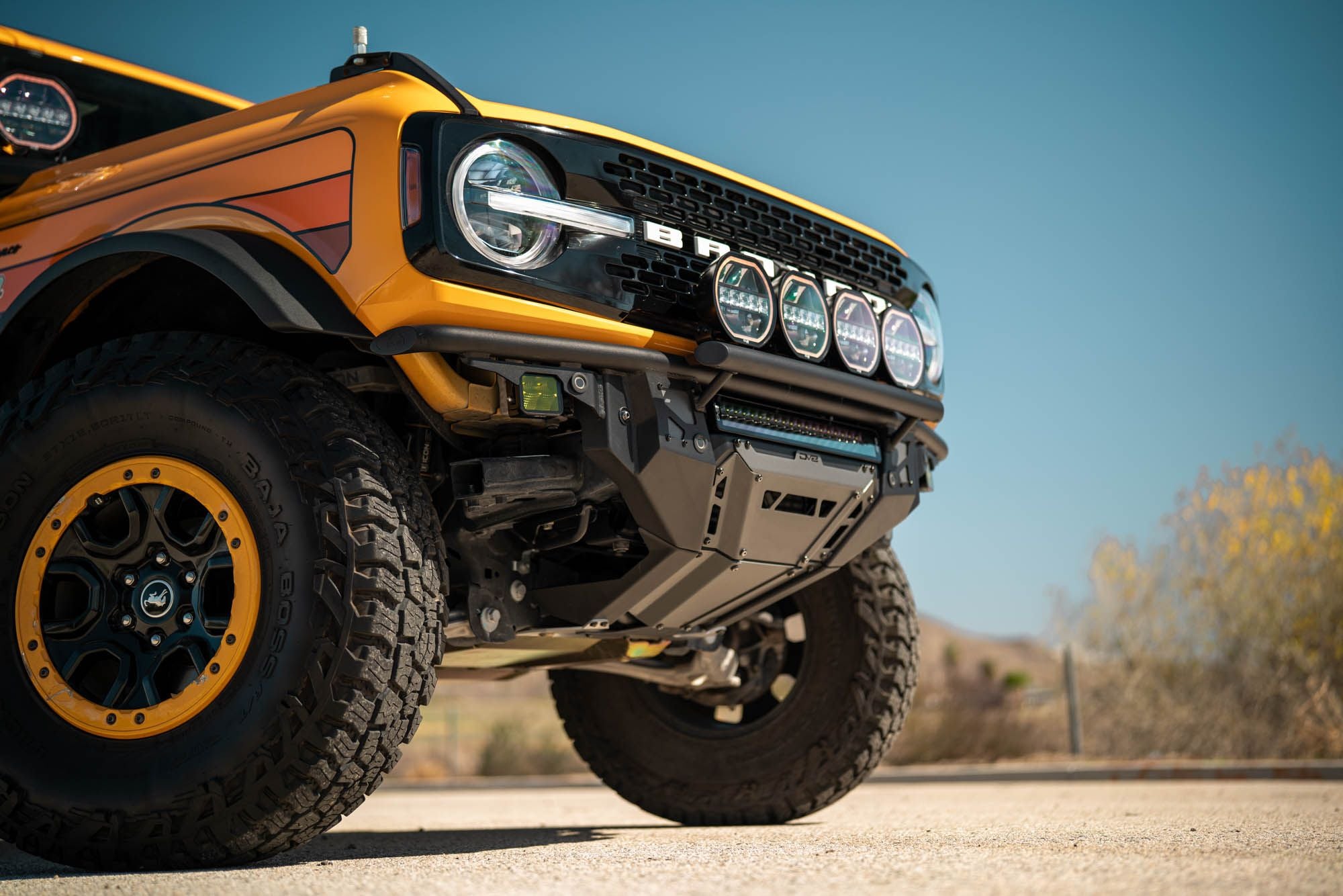DV8 Offroad Tube Series front bumper installed on orange Ford Bronco, close-up front wheel and bumper in desert daylight