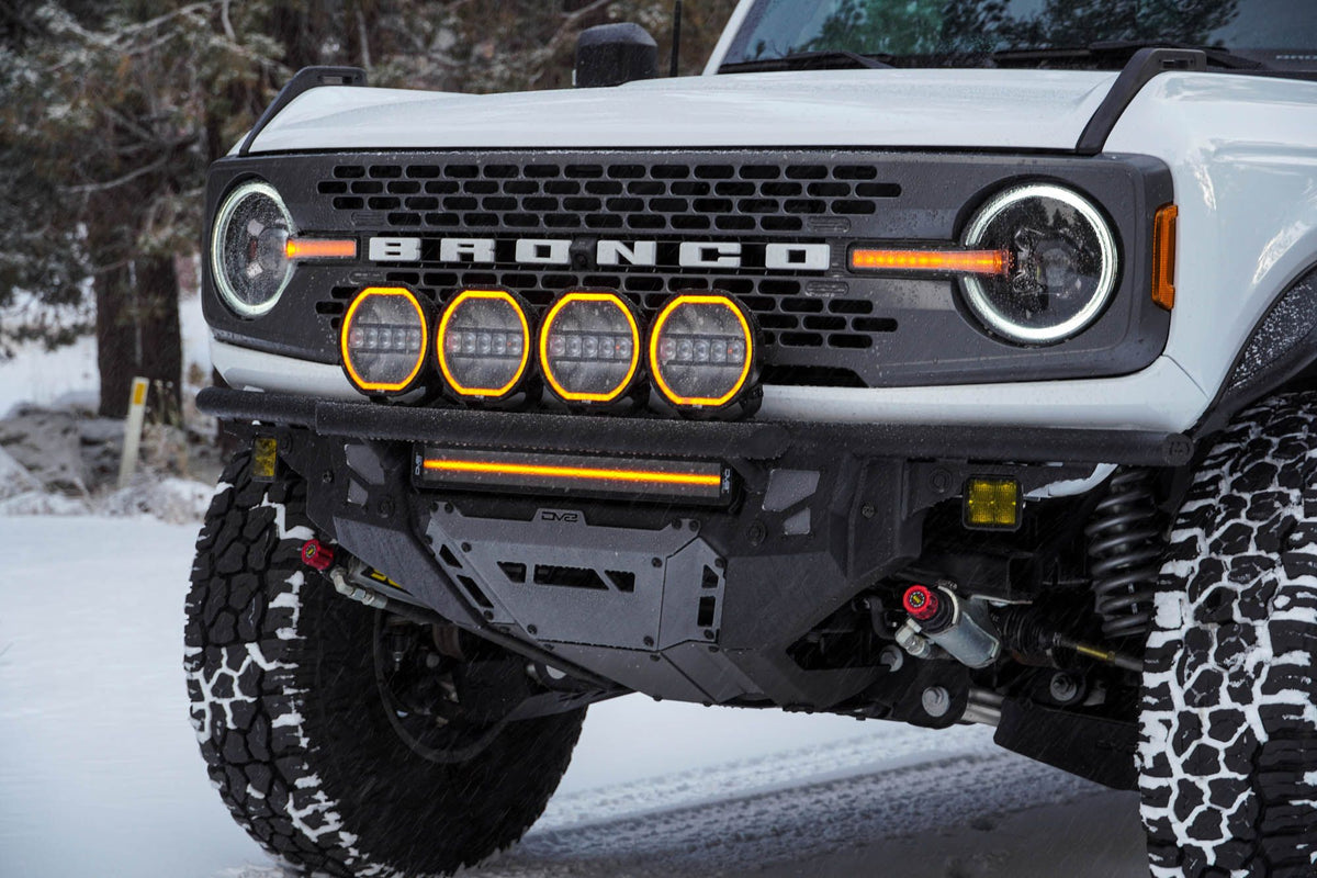 DV8 Offroad Tube Series front bumper installed on white Ford Bronco, close-up front view with round amber lights in snow