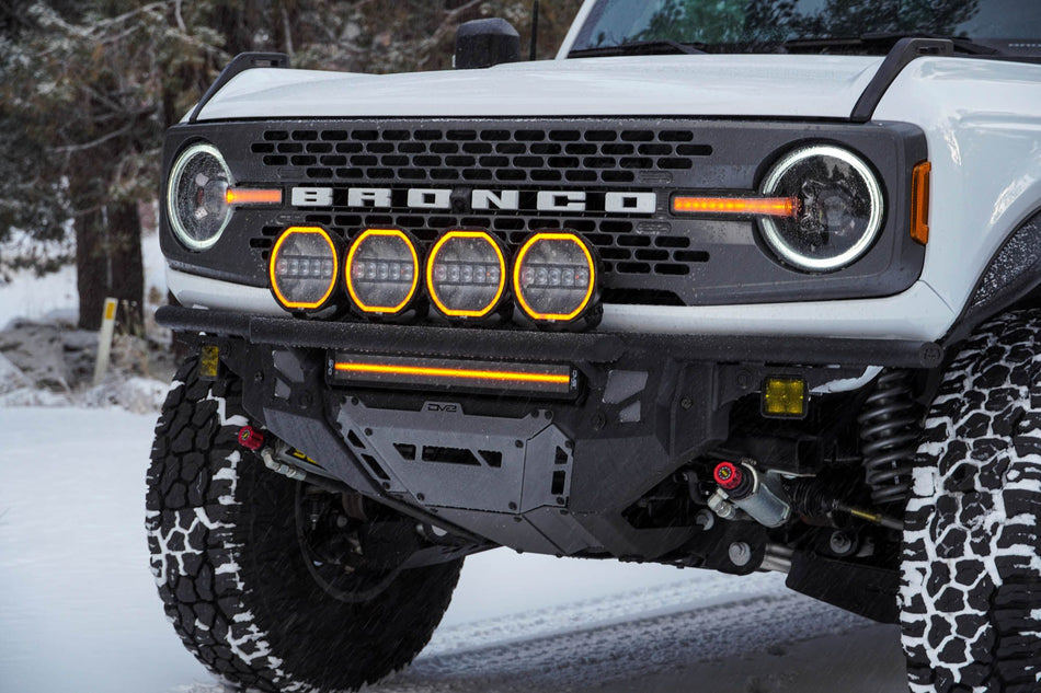 DV8 Offroad Tube Series front bumper installed on white Ford Bronco, close-up front view with round amber lights in snow