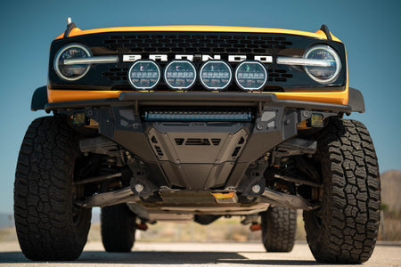 DV8 Offroad Tube Series front bumper installed on orange Ford Bronco, straight-on close-up with round lights, mountain background