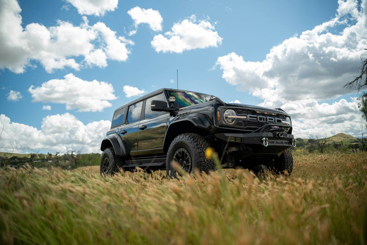 DV8 Offroad Spec Series winch front bumper installed on black Ford Bronco Raptor, distant front three-quarter view with cloudy sky