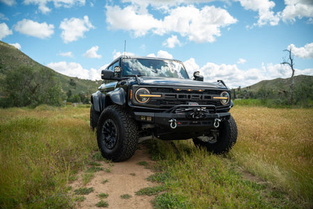 DV8 Offroad Spec Series winch front bumper installed on black Ford Bronco Raptor, distant front three-quarter view on mountain trail
