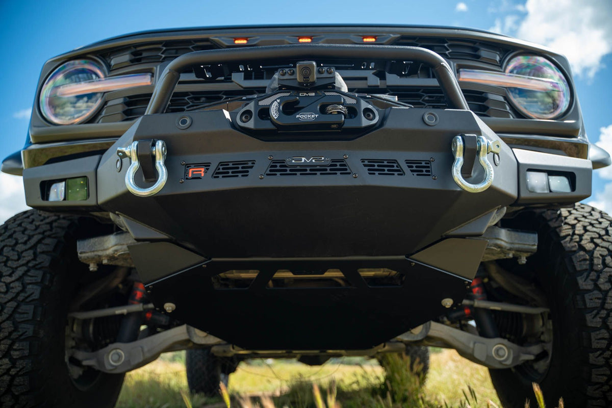 DV8 Offroad Spec Series winch front bumper installed on black Ford Bronco Raptor, low-angle close-up showing headlights and shackles