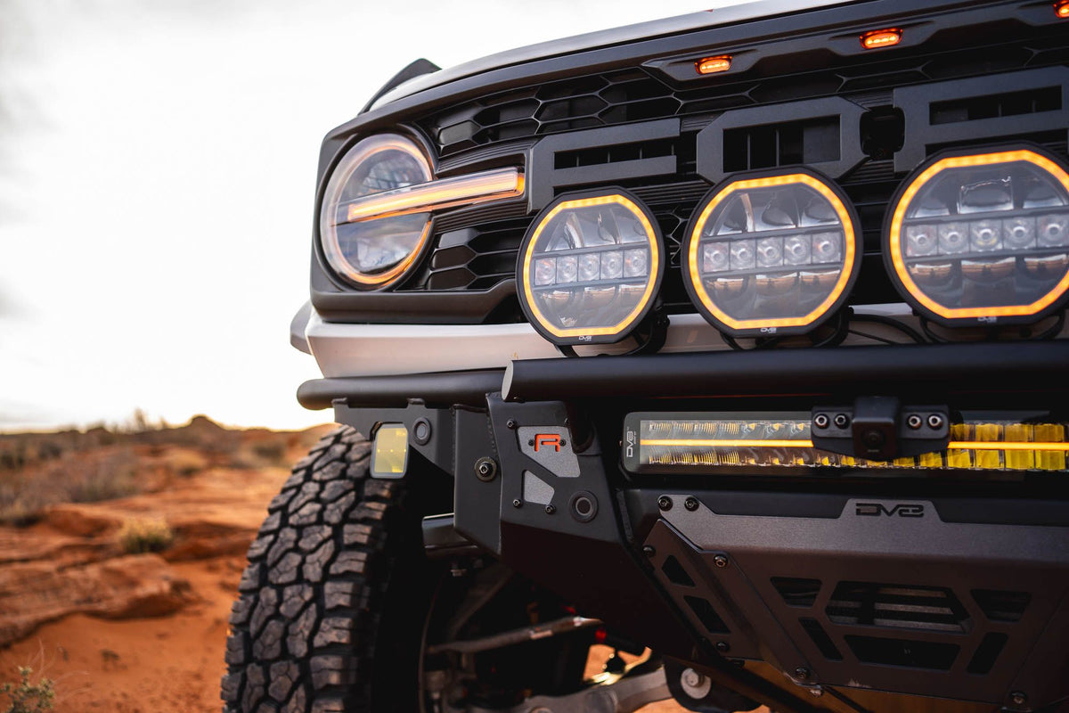 DV8 Offroad Tube Series front bumper installed on dark Ford Bronco Raptor, close-up showing grille and light pods in desert