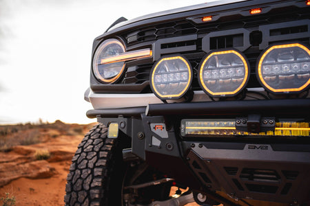 DV8 Offroad Tube Series front bumper installed on dark Ford Bronco Raptor, close-up showing grille and light pods in desert