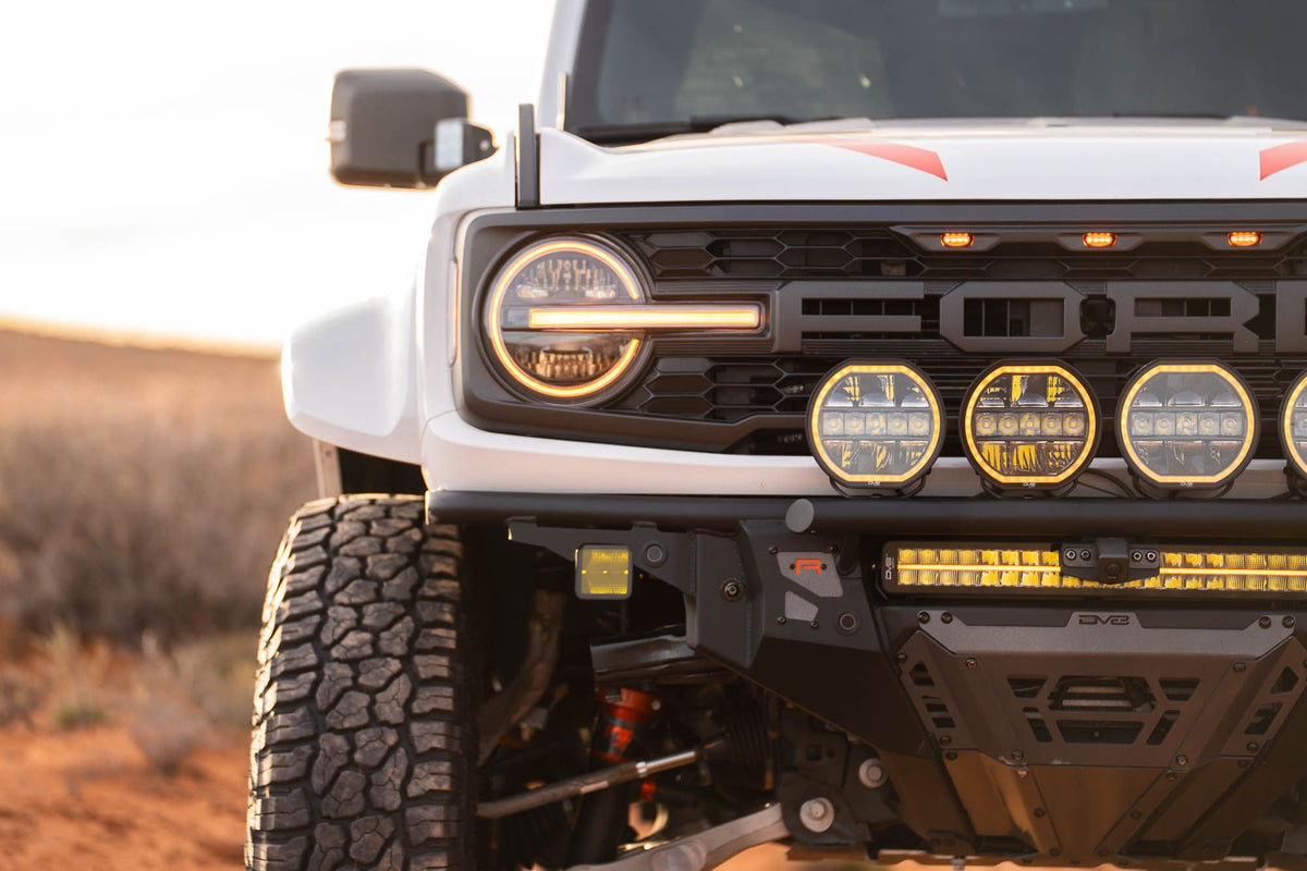 DV8 Offroad Tube Series front bumper installed on dark Ford Bronco Raptor, close-up showing headlight and light pods in desert