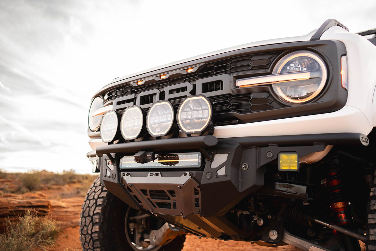 DV8 Offroad Tube Series front bumper installed on white Ford Bronco Raptor, close-up showing grille and light pods in cloudy desert