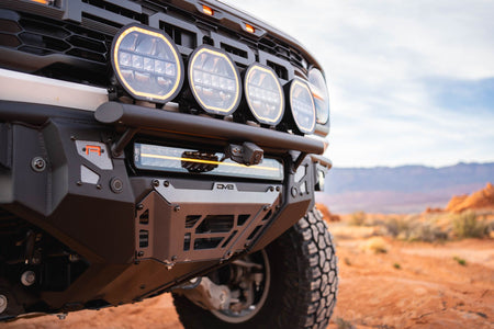 DV8 Offroad Tube Series front bumper installed on tan Ford Bronco Raptor, close-up showing bumper and light pods with desert mountains in background