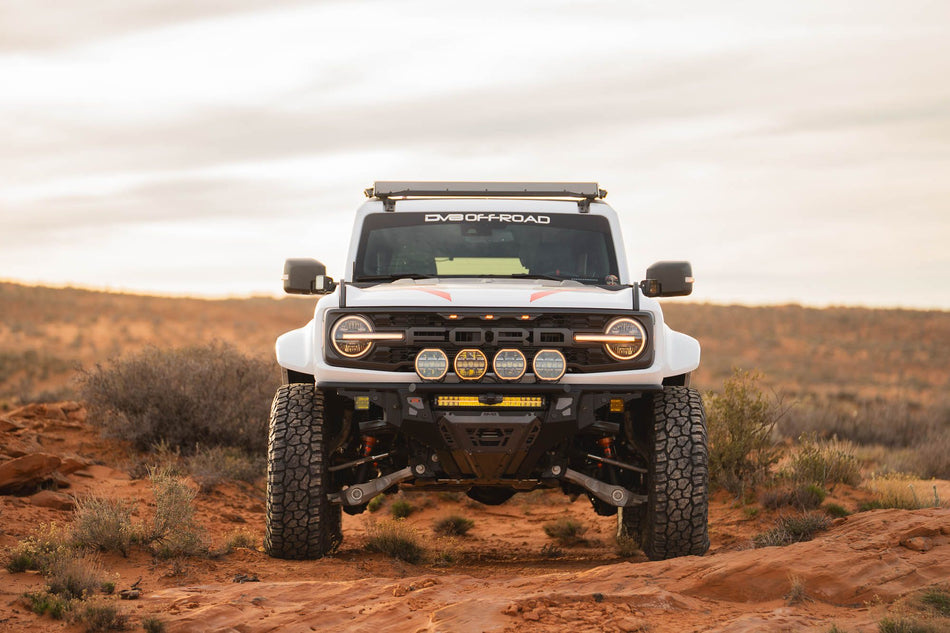 DV8 Offroad Tube Series front bumper installed on white Ford Bronco Raptor, front three-quarter view in desert with cloudy sky