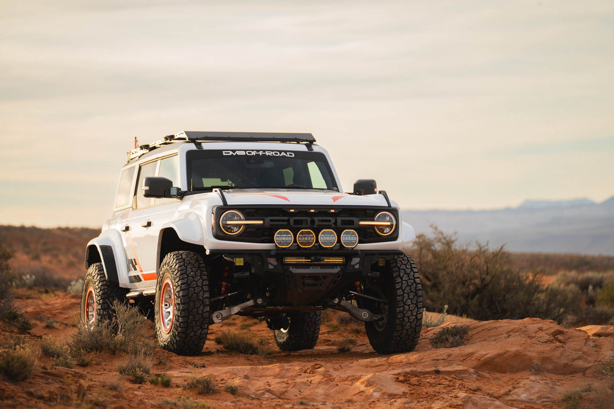 DV8 Offroad Tube Series front bumper installed on white Ford Bronco Raptor with roof rack, front three-quarter view in desert