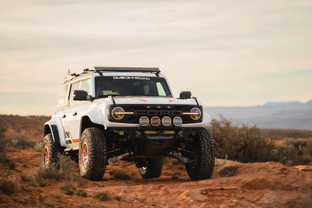 DV8 Offroad Tube Series front bumper installed on white Ford Bronco Raptor with roof rack, front three-quarter view in desert