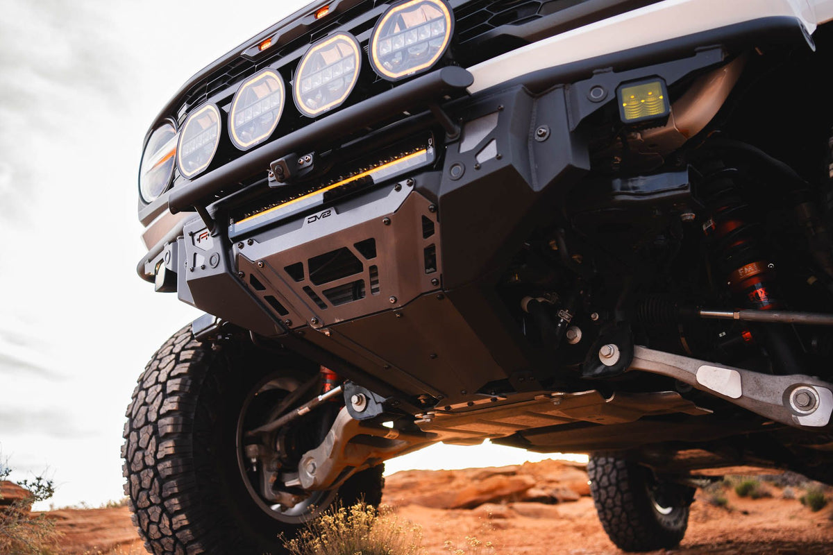 DV8 Offroad Tube Series front bumper installed on tan Ford Bronco Raptor, underside close-up on red rock desert terrain